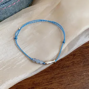 Detail of a light blue woven cord bracelet with a silver fish charm and beads