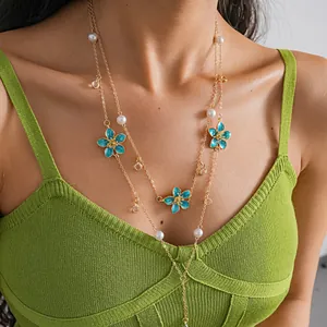 Close-up of layered gold-tone necklace with blue enamel flowers and white pearls on model