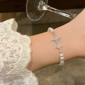 Elegant pearl bracelet with sparkling star charms worn on wrist with lace sleeve.