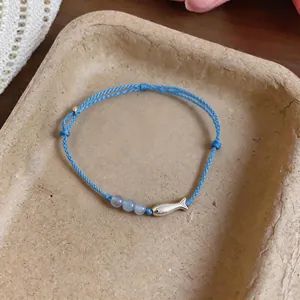Macro view of blue woven rope bracelet with translucent beads and a silver fish charm