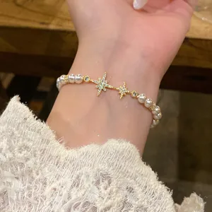 Close-up of elegant pearl bracelet with sparkling cubic zirconia star charms on wrist.