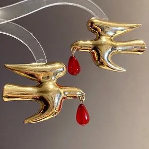 Elegant gold-tone swallow stud earrings with red resin teardrop pendants on a stand
