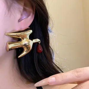Minimalist gold swallow metal stud earrings with a red resin teardrop pendant on model