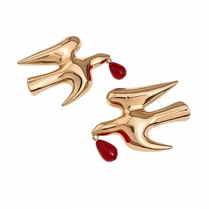 Golden swallow bird earrings with vibrant red resin teardrop pendants on white background
