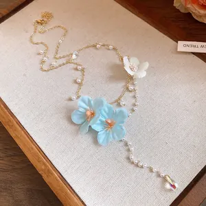 Close-up detail of resort-style gold chain necklace with blue fabric flowers and pearls