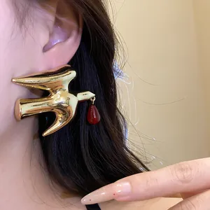 Close-up detail of a gold metallic swallow earring featuring a dark red resin drop