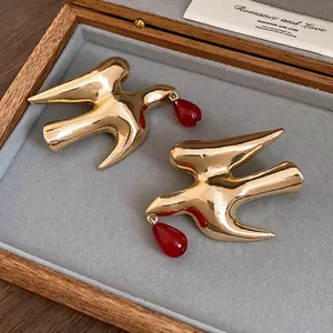 Close-up view of golden swallow stud earrings featuring red resin teardrop pendants