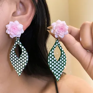 Detail view of stylish pink resin flower earrings with green polka dot drops on model's ear