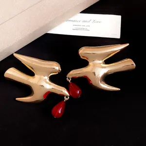 Detailed view of elegant golden swallow earrings with deep red resin teardrop pendants