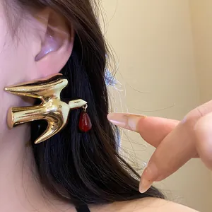 Macro detail of a golden metallic swallow earring featuring a vibrant red resin drop pendant