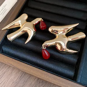 Detailed close-up of golden swallow stud earrings featuring red resin teardrop pendants