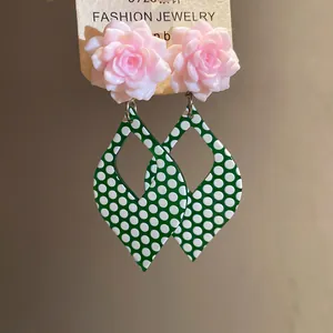 Close-up of elegant pink resin flower earrings featuring green polka dot teardrop pendants.