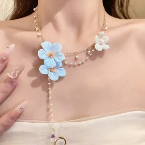Detail of sweet floral necklace with blue fabric flowers and pearls on a model's neck.