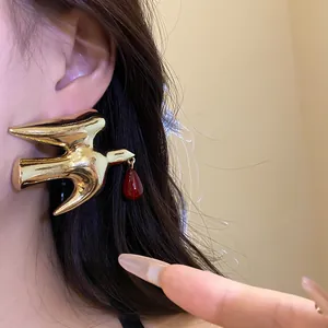 Detailed macro view of golden metal swallow earrings with a delicate red resin drop pendant