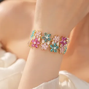 Dettaglio di un braccialetto d'oro a due strati con ciondoli a fiore in zirconi colorati.