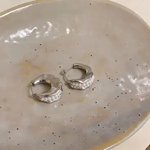 Detailed view of silver geometric hoop earrings with pearl inlay on a ceramic plate