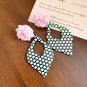 Detail view of pink resin flower earrings with green polka dot rhombus drops on wood