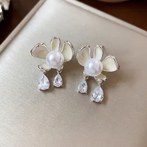 Elegant flower pearl stud earrings with pear-shaped crystal drops on champagne background.