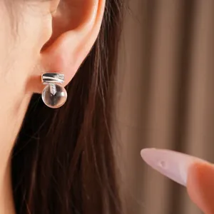 Close-up view of a minimalist round clear resin stud earring worn on a model's ear