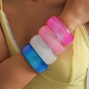 Detail view of colorful glittery iridescent resin bangles on wrist, dopamine style