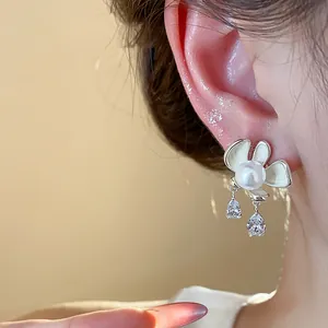 Elegant flower pearl stud earrings with enamel petals and crystal drops on model's ear