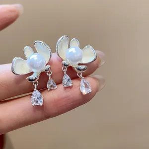 Close-up of elegant flower stud earrings with pearl and dangling pear-cut zircons.