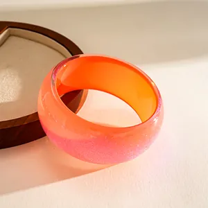 Detail view of a chunky resin bangle with orange and glittery pink gradient.