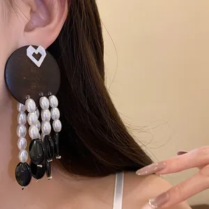 Close-up view of vintage style wood and pearl tassel earrings worn on ear for detail display
