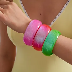 Close-up of three vibrant glitter resin bangles in pink, red and green worn on a model's wrist