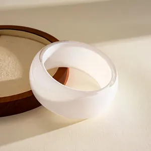 Detail view of a white resin bangle with subtle iridescent glitter on a wooden stand.