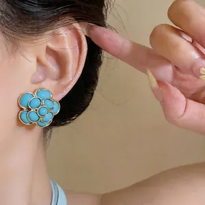 Elegant vintage turquoise resin flower stud earrings with gold trim shown on ear