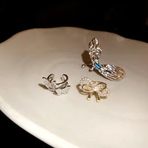 Nahaufnahme von elegantem Schmetterling-Ohrclip und goldener Schleifenperle auf Keramikteller