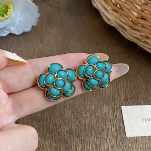 Close-up of French vintage teal resin flower stud earrings held between fingers