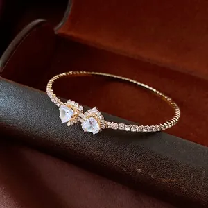 Elegant gold open cuff bangle featuring two heart-shaped crystals on a dark backdrop