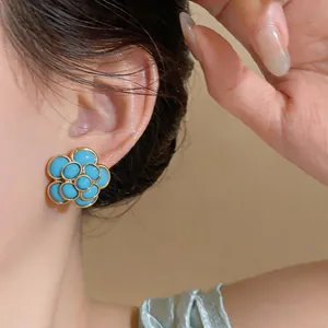 Close-up detail of elegant blue floral resin stud earrings with vintage gold finish