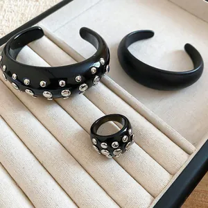 Close-up of luxury black resin bangle and ring set with silver studs in a jewelry tray.