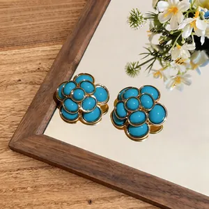 Close-up of vintage resin flower stud earrings with cyan oval stones and gold frame