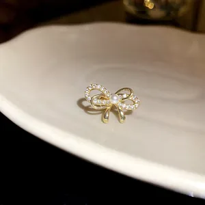 Detailansicht eines goldenen Ohrclips mit Zirkonia-Schleife und Perle in der Mitte.