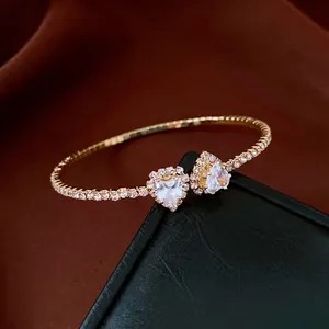 Elegant gold-plated open bracelet featuring two sparkling heart-shaped crystals and rhinestones