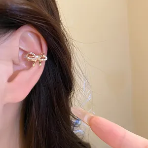 Detailansicht einer glitzernden Zirkonia-Bogen-Ohrklemme mit Perle am Ohr einer Frau.