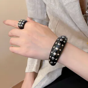 Detailed macro view of black resin bangle and ring set with silver stud embellishments.