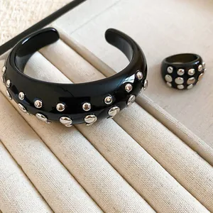 Close-up detail of black resin cuff bracelet and matching ring set with silver-toned studs