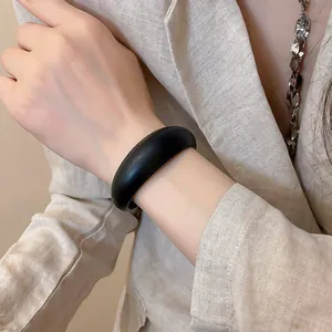 Detail of a minimalist black resin open bangle on a model's wrist with linen blazer.