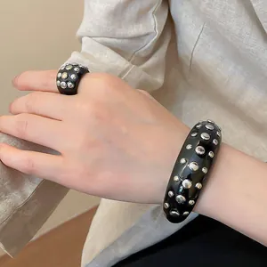 Close-up of a black resin jewelry set with silver studs on a hand wearing a shirt