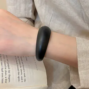 Detailed view of a matte black resin oval cuff bracelet paired with cream linen fabric.