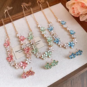 Zircon flower earring and necklace sets in pink, green, and blue on a wooden tray