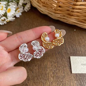 Orecchini a perno in zircone placcati oro 18K con design cavo e perle, tenuti in mano.