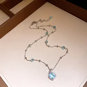 Detail of elegant silver necklace with light blue square pendant and sparkling zircon halo