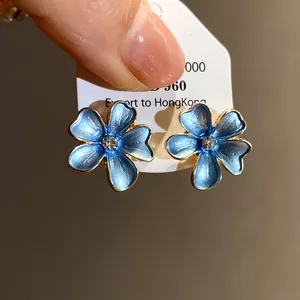Close-up detail of blue spray-painted flower stud earrings with a clear central zircon stone