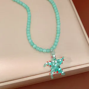 Macro view of a detailed teal glass starfish pendant on a light blue beaded necklace chain